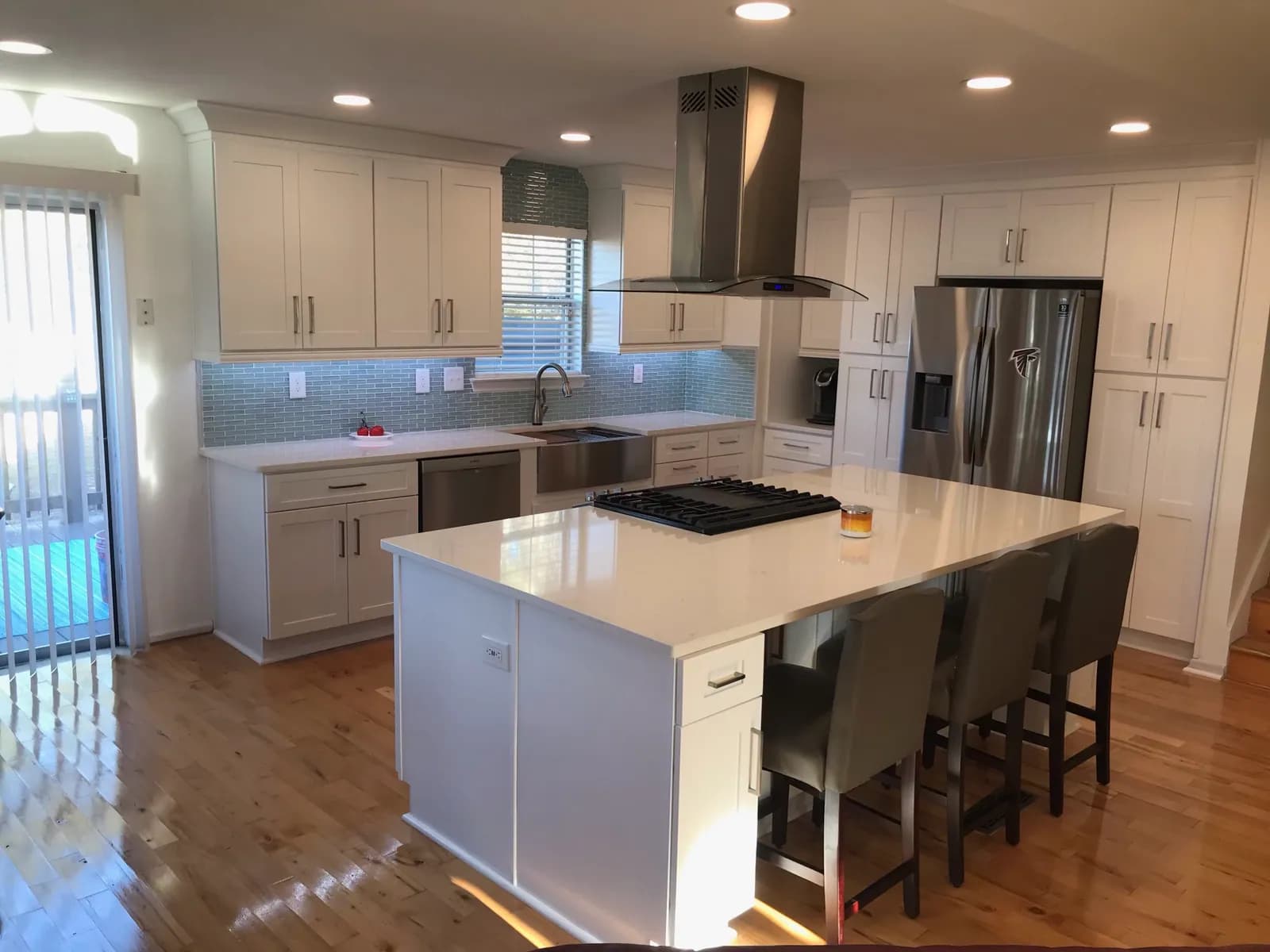 Bright white shaker kitchen with aqua glass tile backsplash and island cooktop