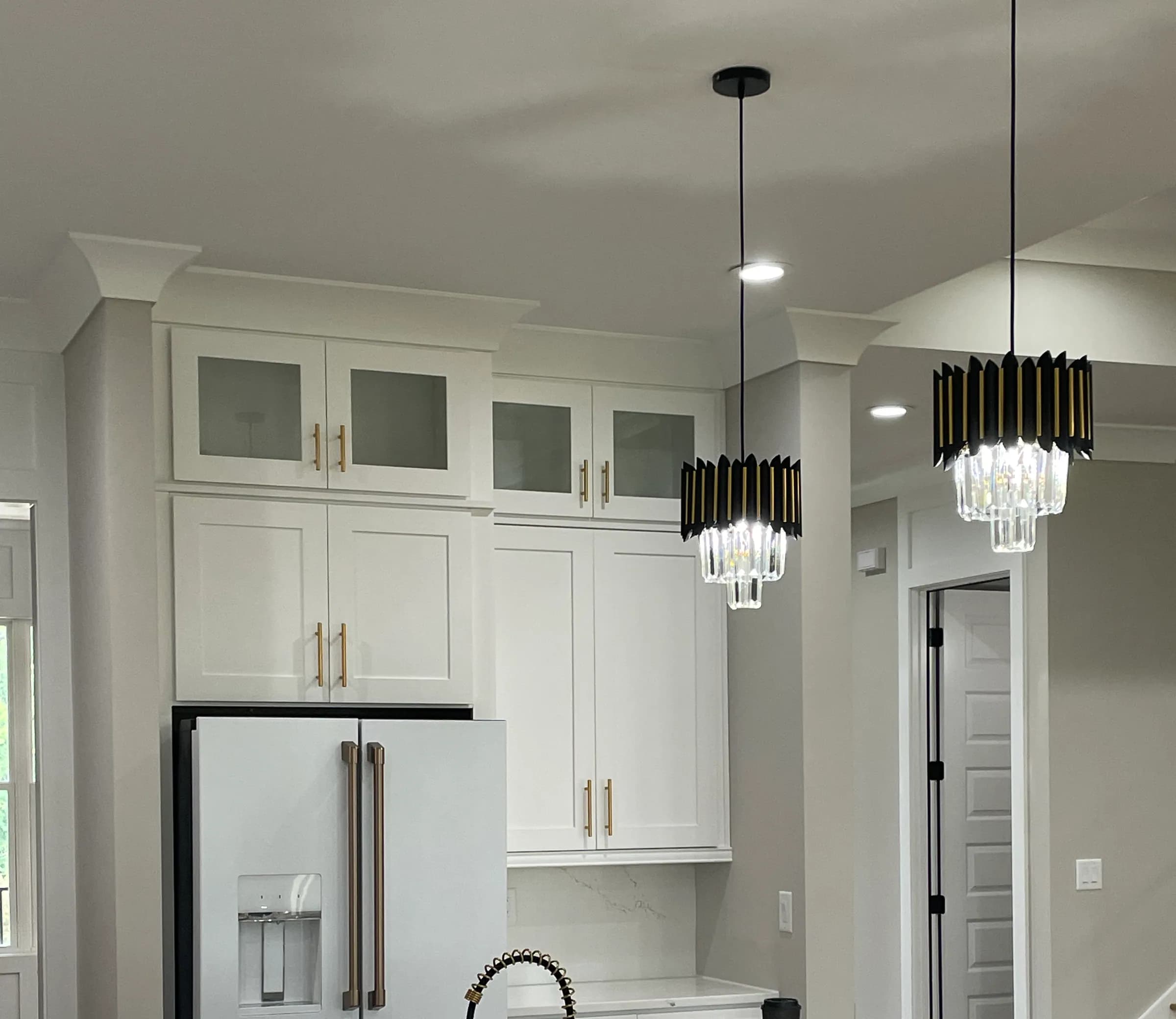 White cabinets with brass hardware, apron-front sink and black-and-gold crystal pendants