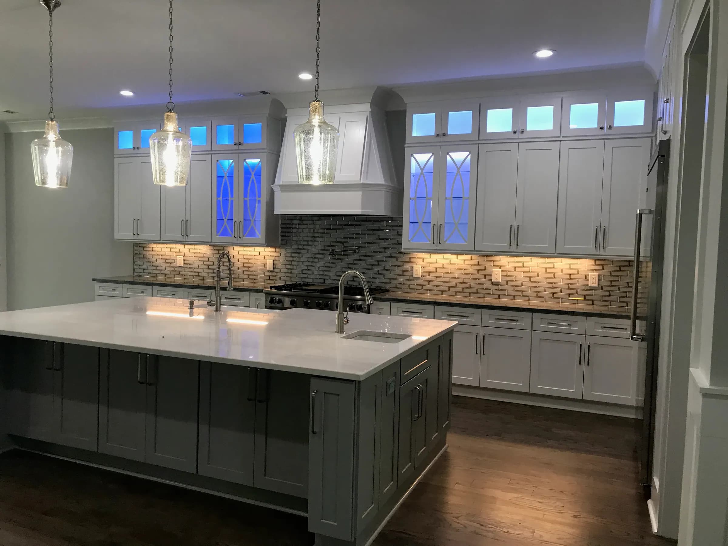 Mullion glass upper cabinets with blue LED lighting over a grey island