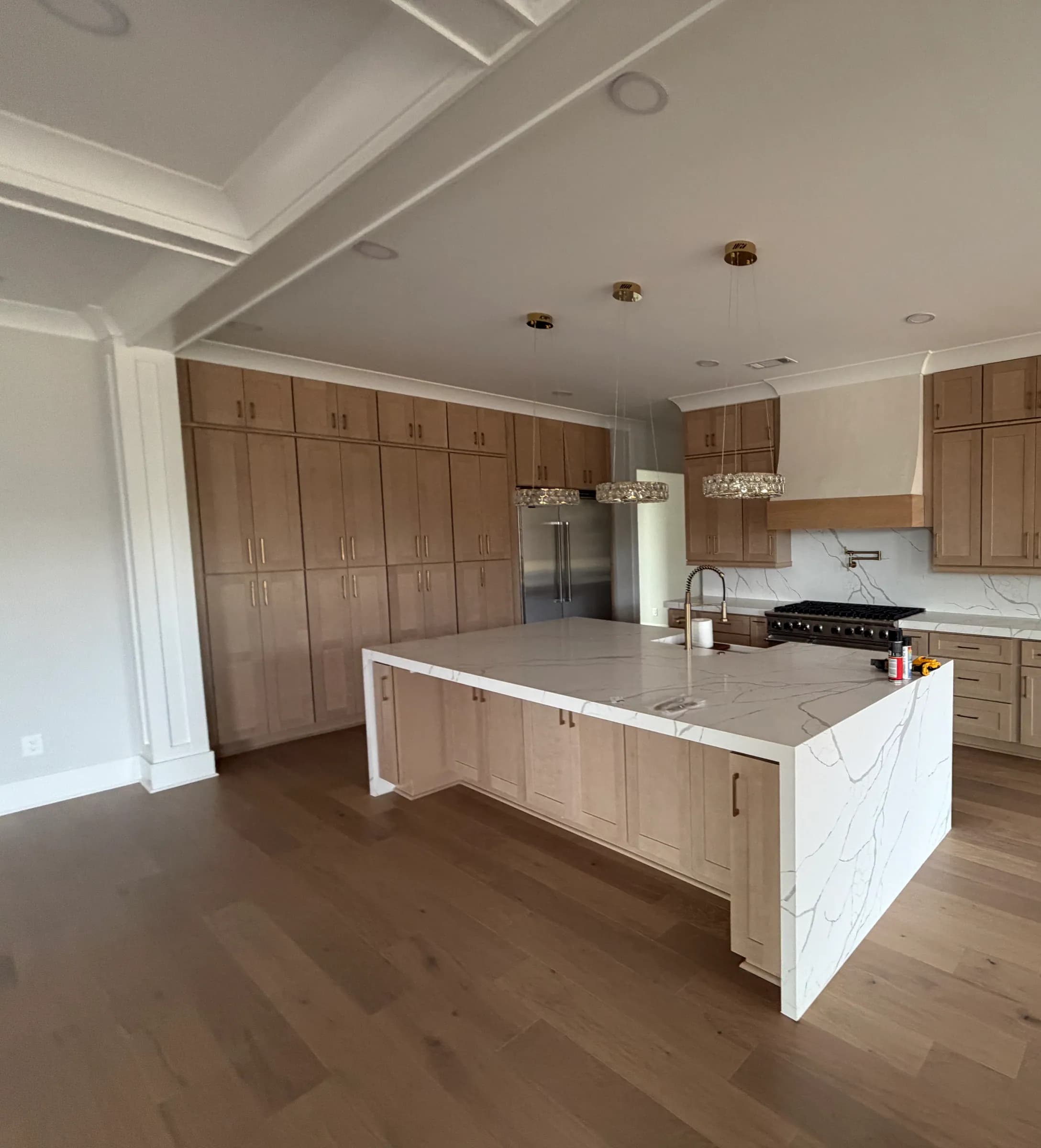 Floor-to-ceiling natural oak cabinets with a white quartz waterfall island