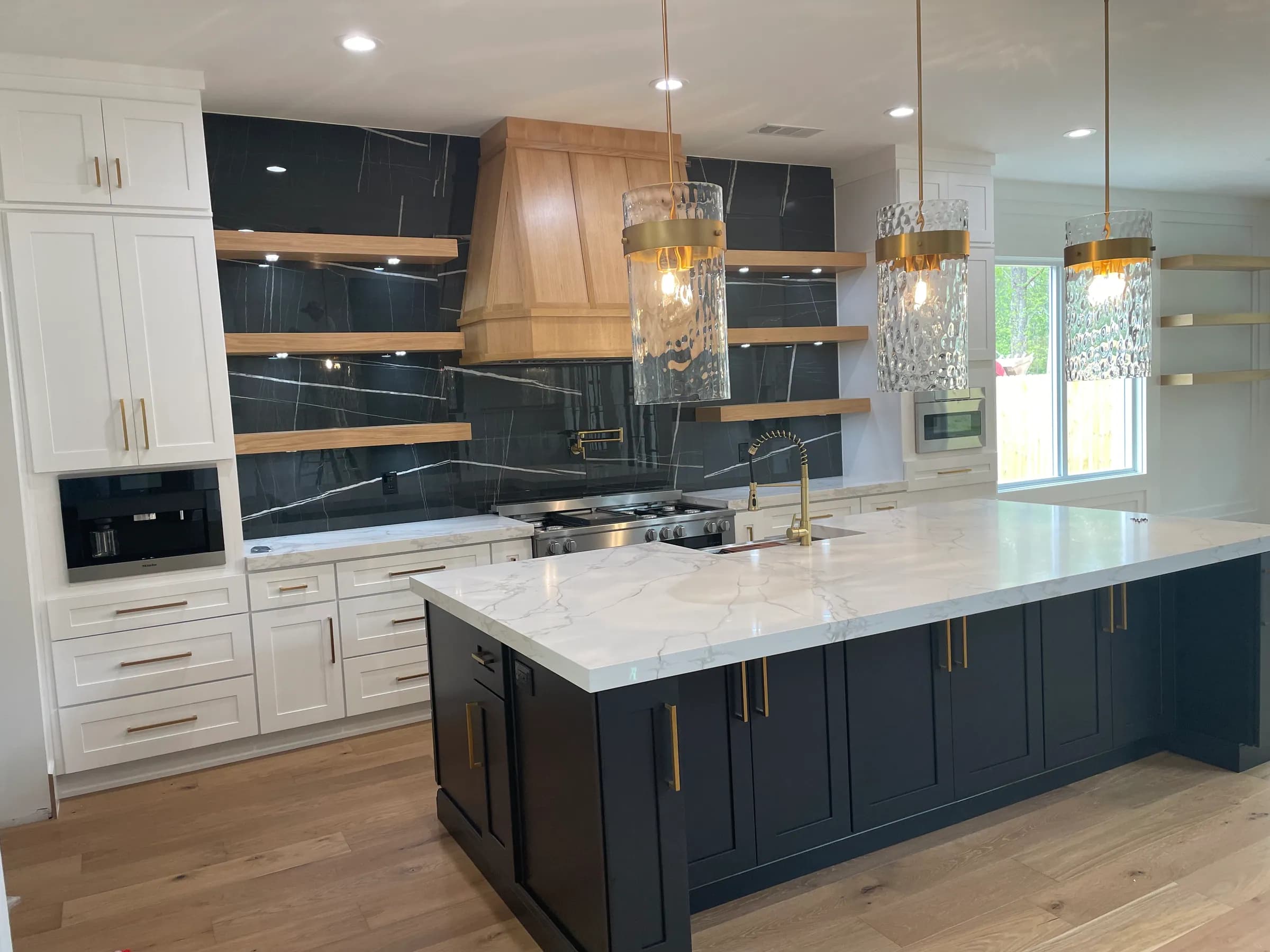 Navy island, black marble slab backsplash, floating oak shelves and built-in coffee machine
