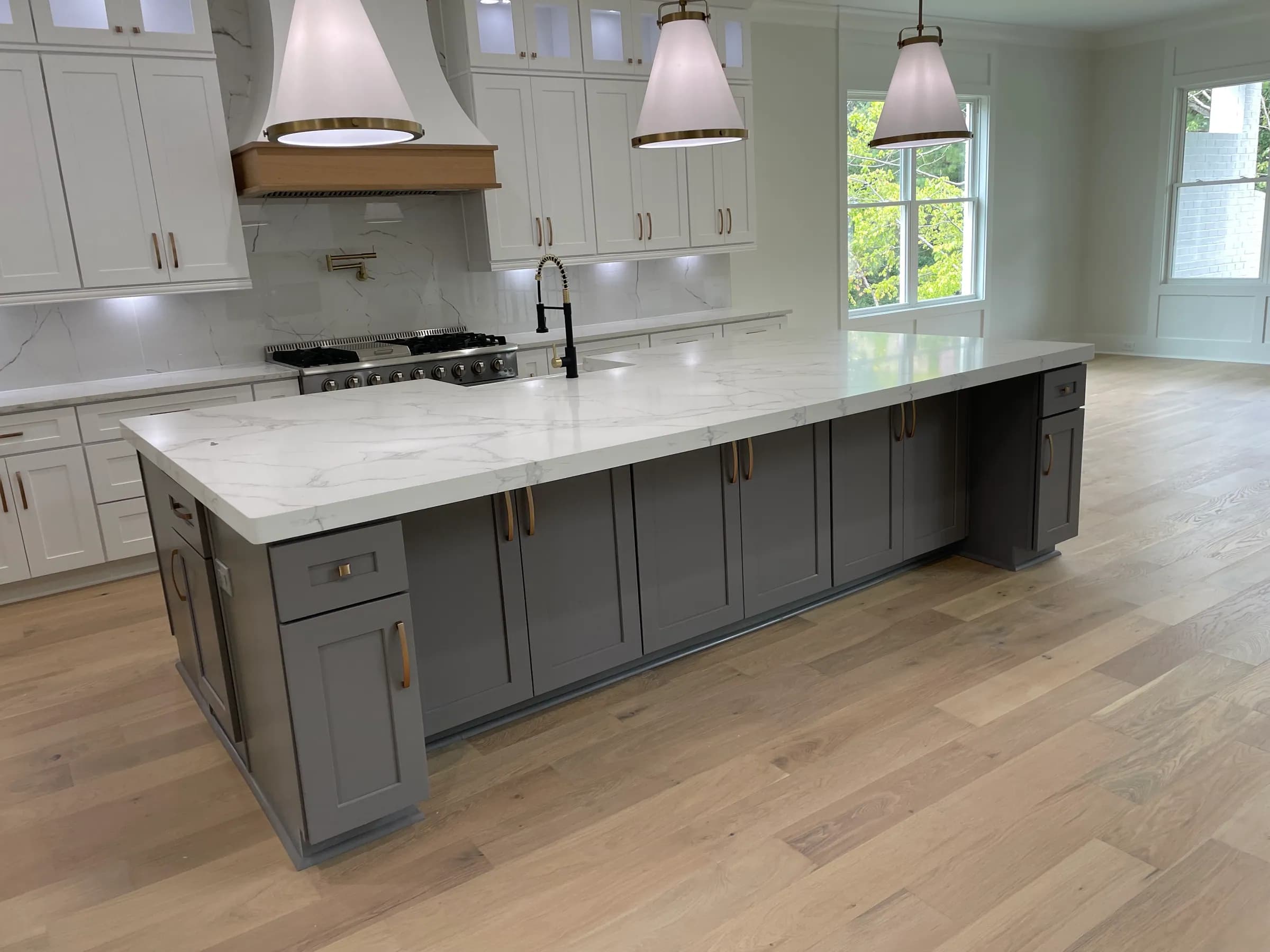 White shaker cabinets, grey island with waterfall quartz, oak-banded range hood and brass fixtures